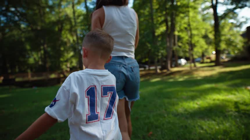 Child in a white number 17 shirt walks hand in hand with a woman on a lawn