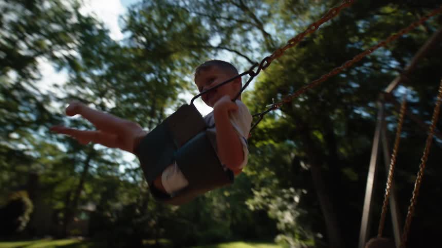 Two children swing on a swing set while two adults stand behind them