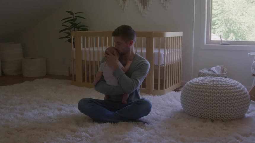 Father carries and kisses his child while sitting on the floor in a bedroom during daytime