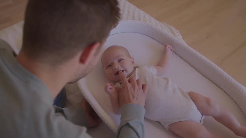 Man sitting next to a crib caressing a smiling baby indoors during day time