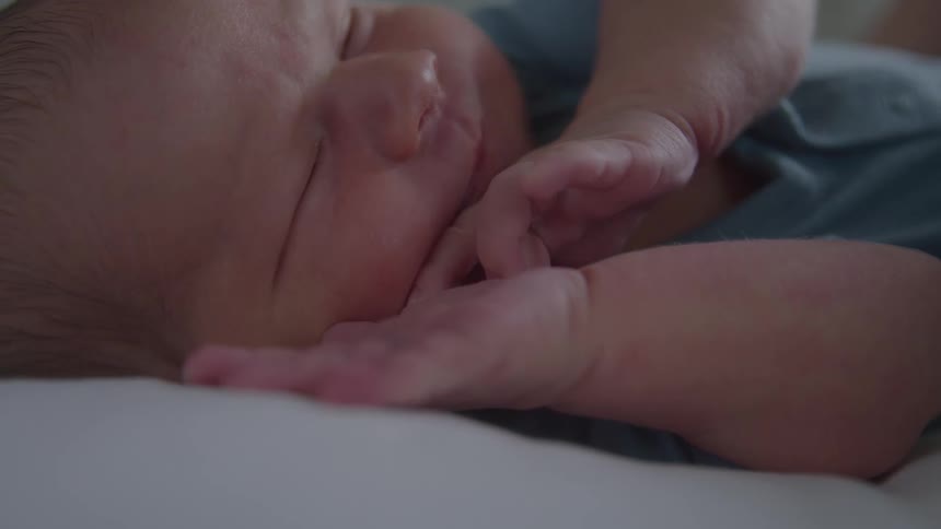 Newborn lying down with eyes closed and hands near the face
