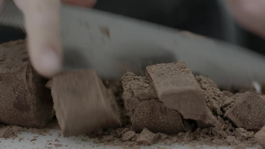 A chef is cutting up chocolate with a knife