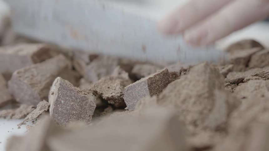 A person is chopping chocolate pieces with a blade