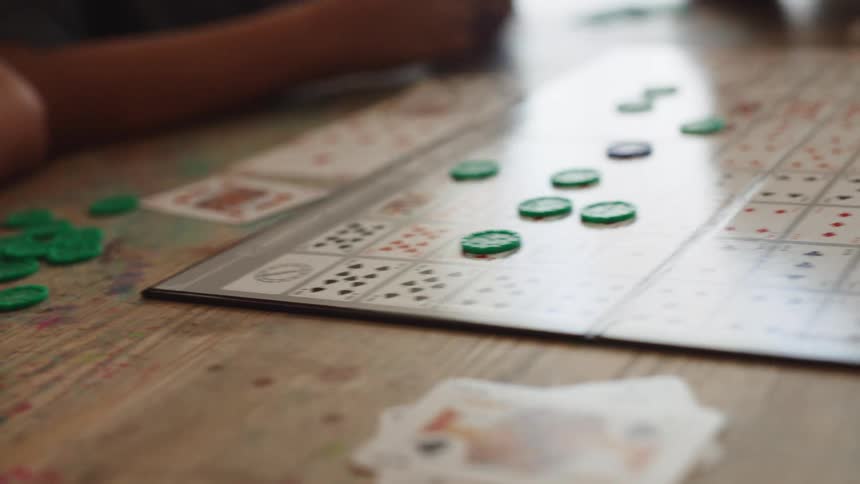 Two boys are playing a board game using green tokens at a table