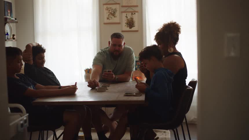 A family of five play card games while sitting at a table indoors during daytime