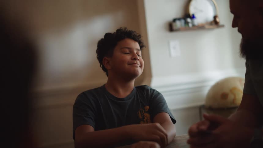Boy sitting at table chatting with other people in a cheerful manner