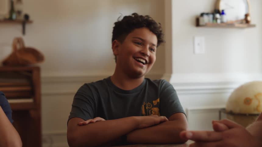 Two boys sitting at a table laughing while talking to other people