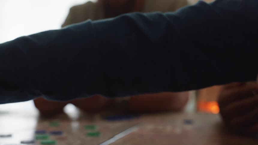 Three people indoors playing a game of cards over a wooden table during day time
