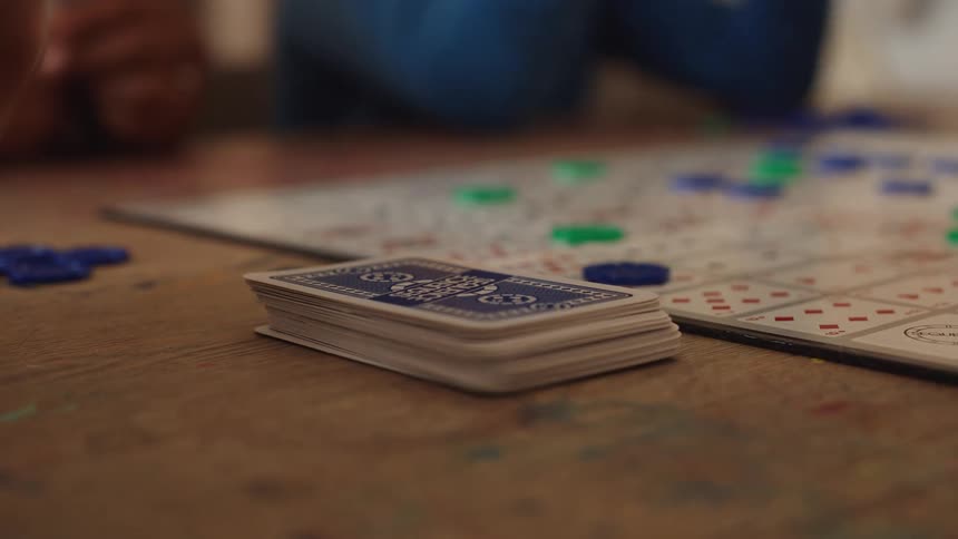 People playing cards on top of a wooden table indoors during day time