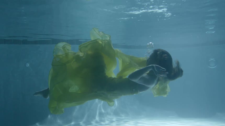 Woman underwater in a pool wearing a yellow gown