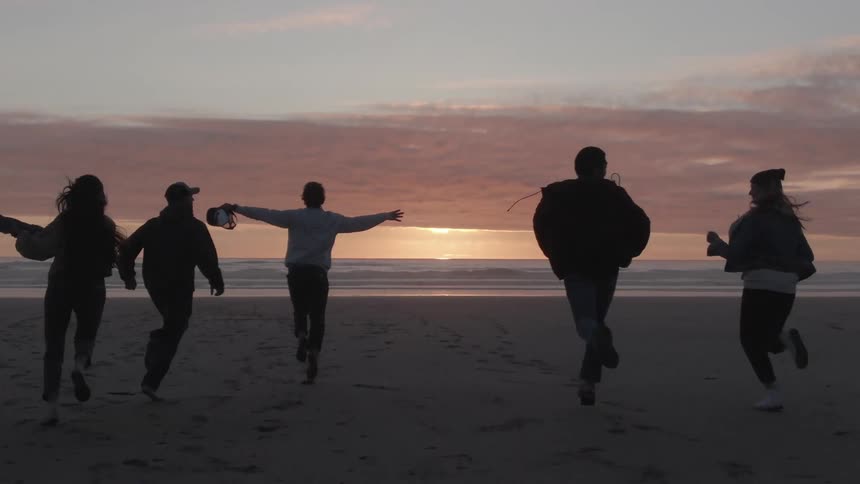 A group of people runs on a beach during the sunset while the ocean waves roll onto the sand