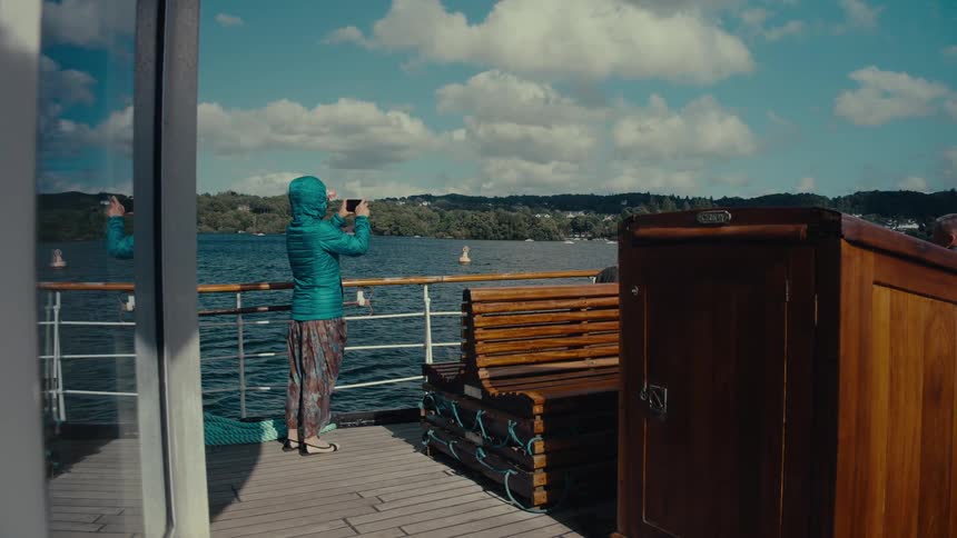A person taking a photo while standing on a boat deck overlooking the water