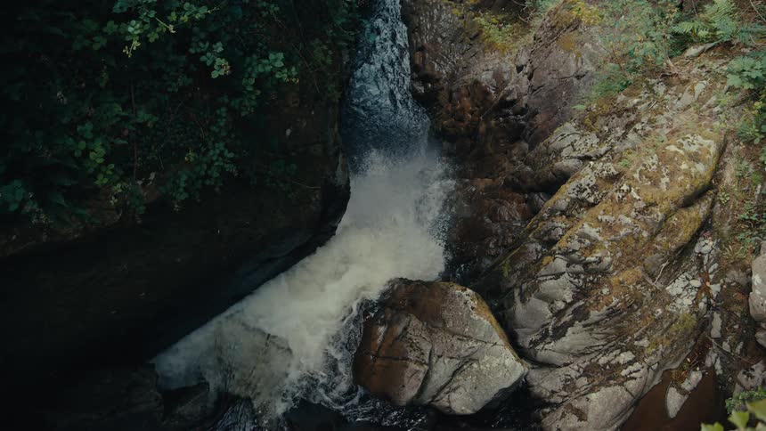 A powerful waterfall cascades down a rocky crevice surrounded by lush green foliage and mosscovered stones the water crashes into the basin below creating a foamy churning pool before flowing onward