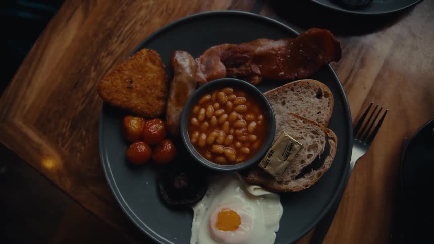 A persons hand puts a fork next to a plate with healthy food on a wooden table