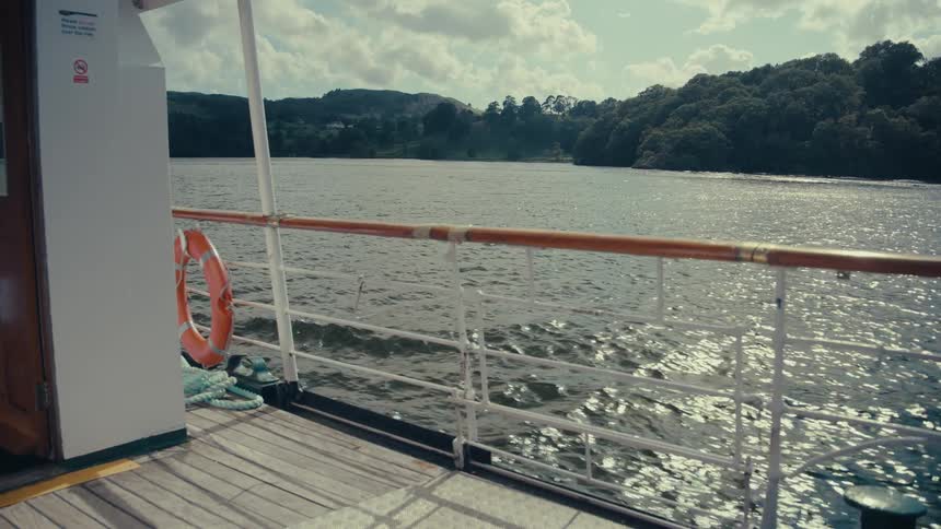 A shot from a boats deck shows the waters surface as the boat moves along the water reflects sunlight creating a shimmering effect