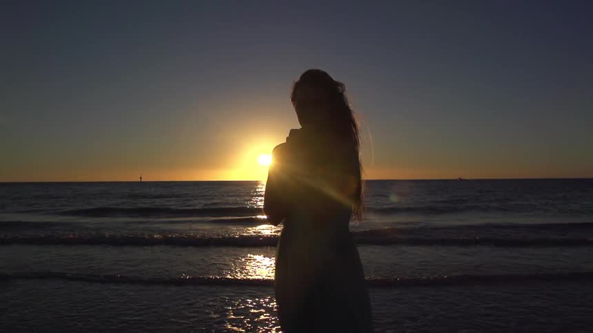 Woman standing in front of ocean at sunset