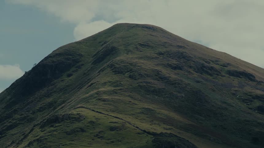 A grassy mountain peak rises under a cloudy sky