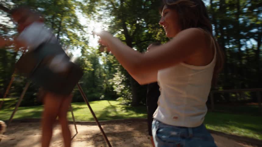 A family of four at a park with the mother and father pushing their two children on swings next to one another