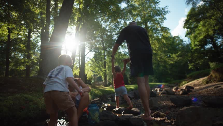 A family of four play around a stream in the middle of the forest