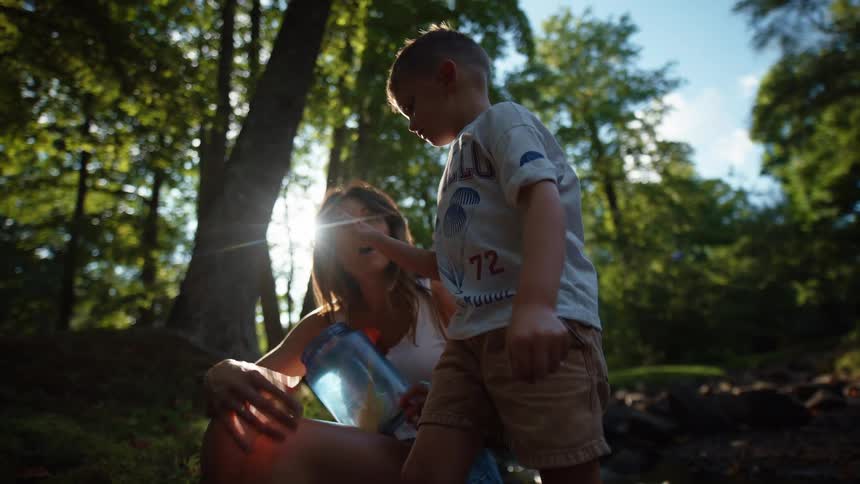 A family is gathered in a shallow sunlit stream where a woman and a young boy are crouched down