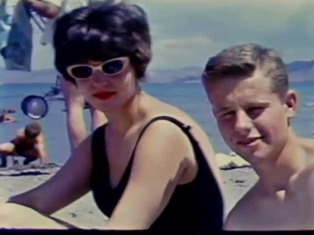Woman and boy sit at a crowded beach on a sunny day