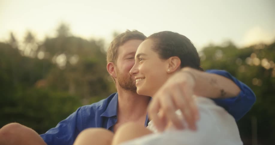 A man and a woman sit together and embrace while looking at something offcamera