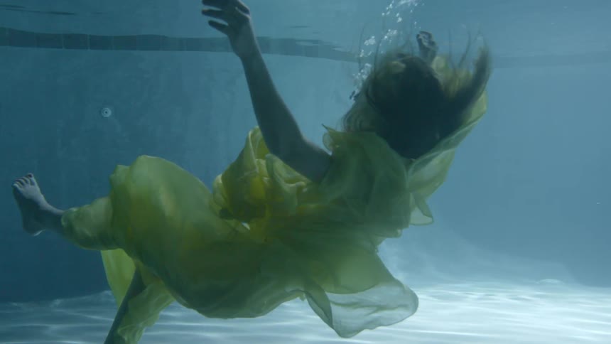 A woman wearing a yellow dress falls underwater