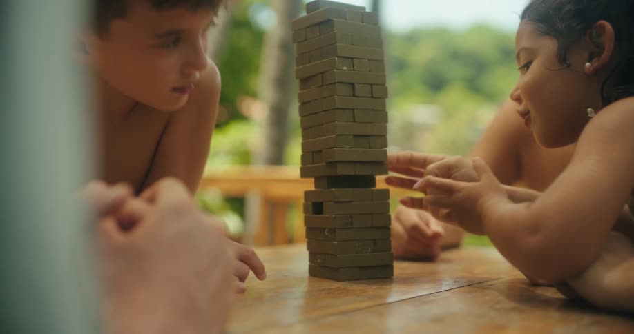 Children play jenga together at a wooden table outdoors