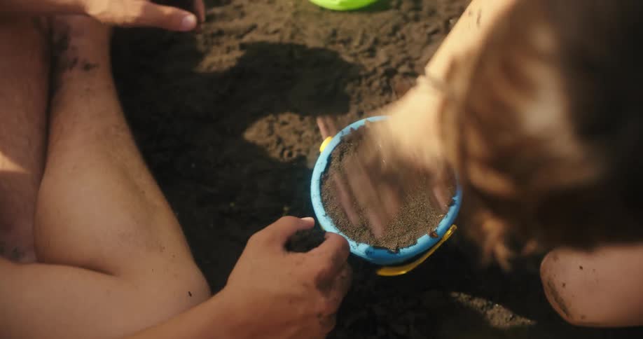 Father and son patting wet sand into a bucket at the beach