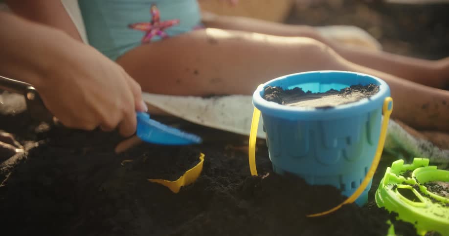The girl digs and fills the pale with black sand