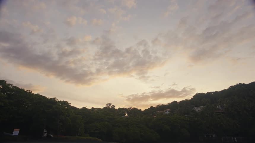 A soft sunset sky glows above a green hillside with houses