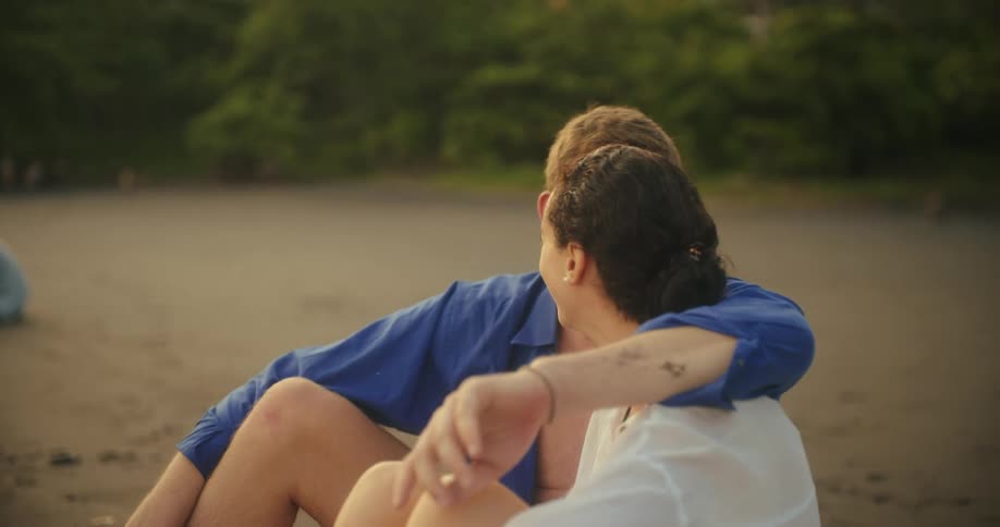 A couple sits close together having an affectionate conversation on the beach