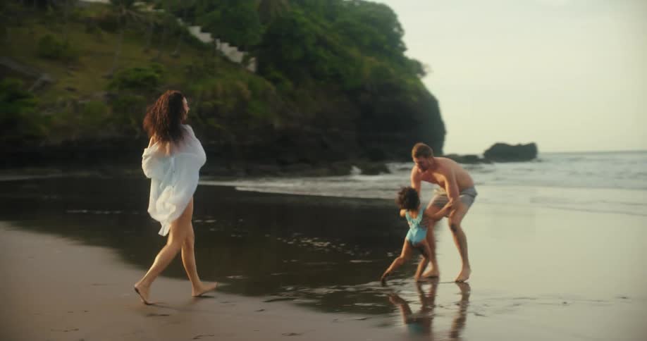 A girl runs over to her father on the beach and he lifts her up