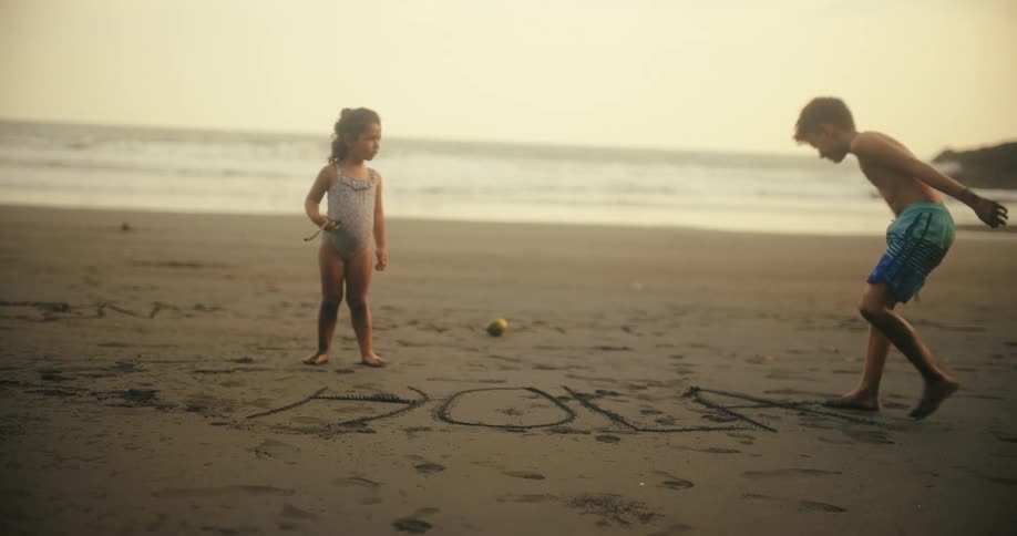 A boy is tracing a word into the sand