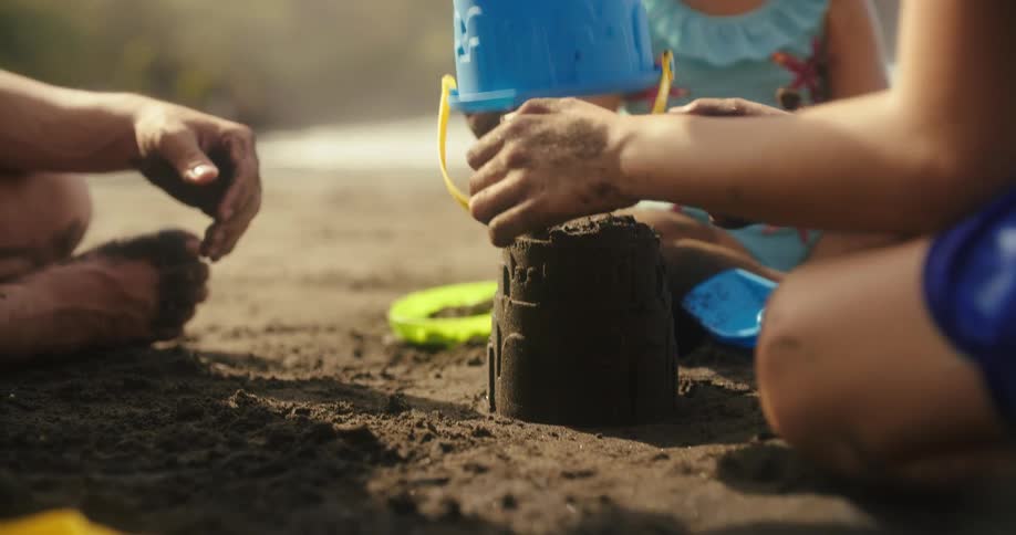 Children playing in the sand with a bucket and beach shovels