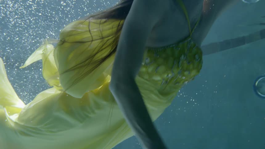 A woman in a gown swims underwater in a pool