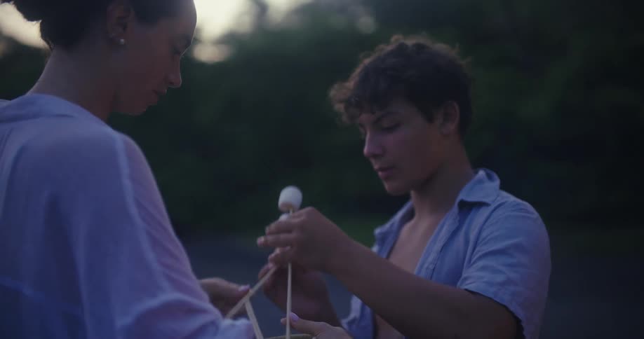 Teenagers are standing outside as they put marshmallows on thin sticks
