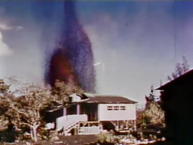 Lava erupts into the air behind a house
