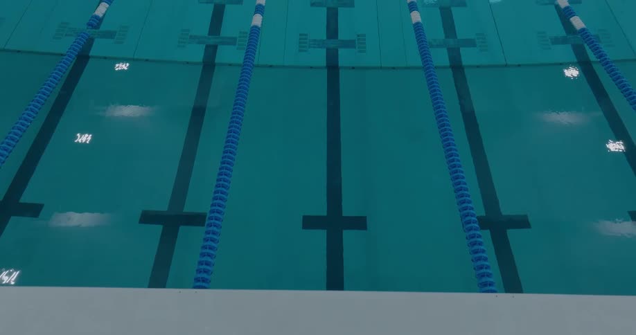 An aerial view shows a swimming pool with dark blue lines on the bottom and several blue and white lane dividers floating on the surface