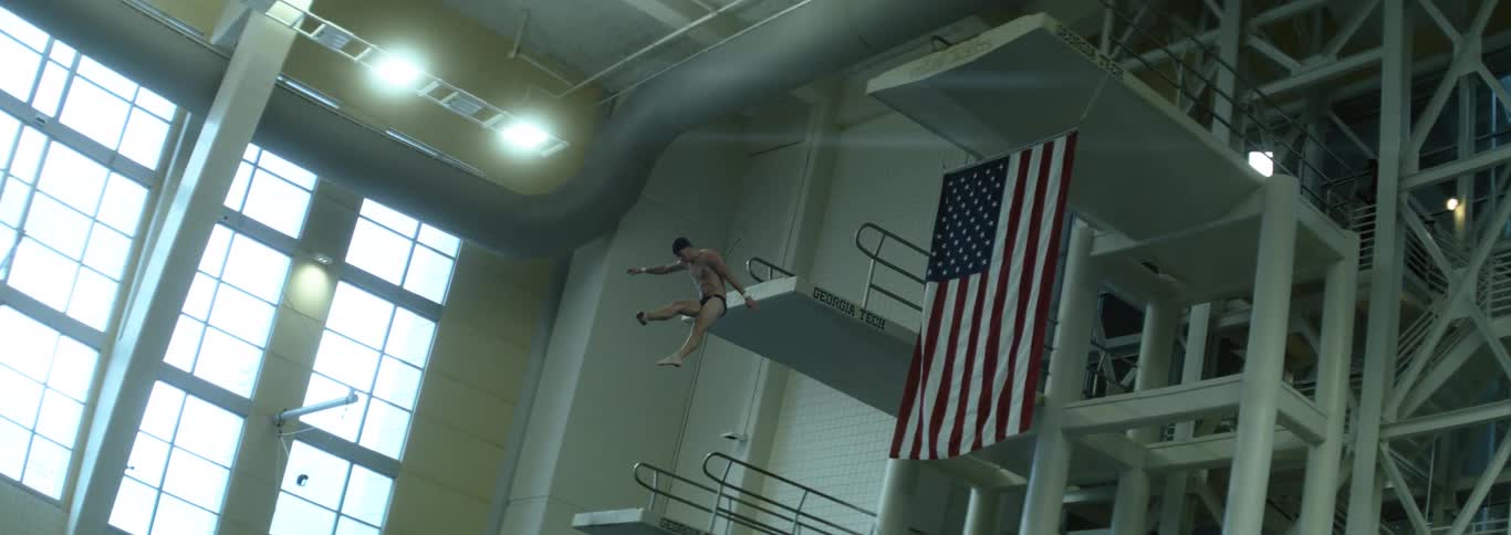A man jumps off of an indoor high dive and rotates as he dives