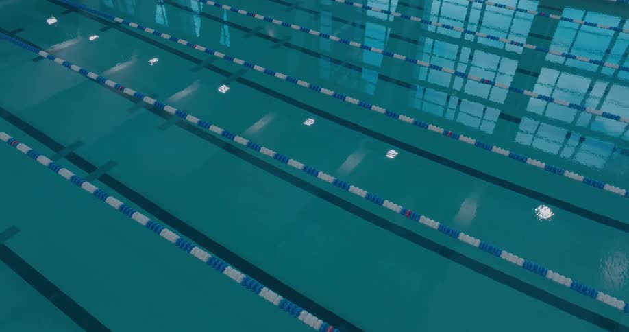 The camera looks down at the water in a swimming pool showing the lanes and the ripples on the surface