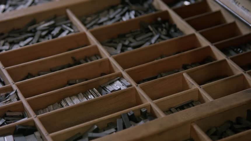A man opens a drawer that is filled with letters for a vintage printing press