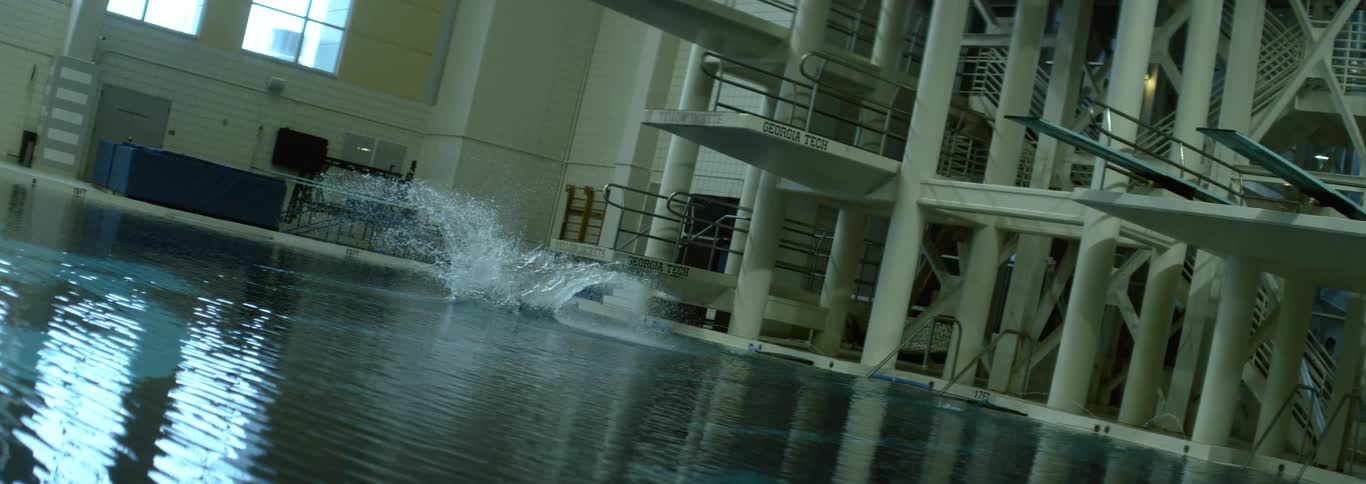 Female athlete dives off a diving board into an indoor pool during the daytime