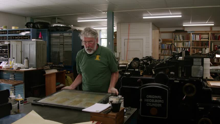 An elderly man in an office carrying a nameplate and placing it on a desk