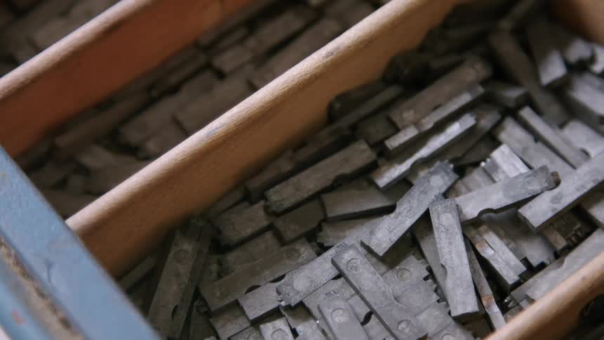 Metal printing type pieces are stacked inside a wooden compartment tray