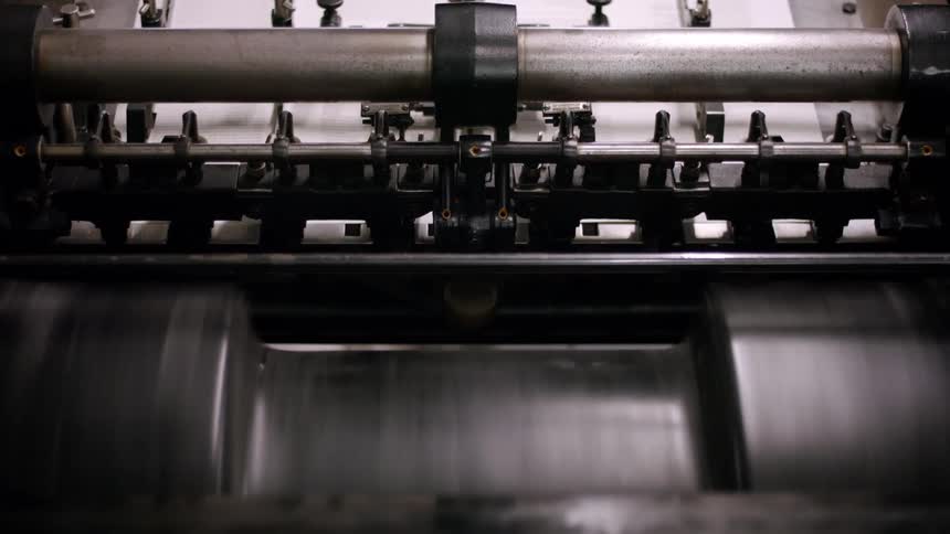 A large piece of white paper is being pulled into a printing press then quickly and smoothly fed through the machine the industrial press is shown in a closeup shot highlighting its fastmoving metallic parts
