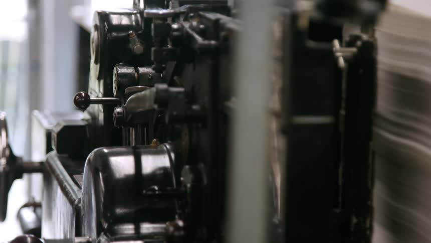 A shot focuses on the intricate rhythmic motion of a vintage printing press metal arms and rollers work in tandem to process a stack of paper