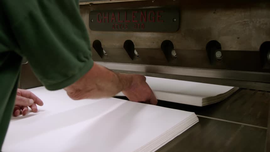 A man arranges blank white papers in a cutting machine