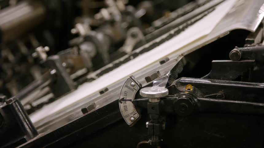 An older mechanical printing press repeatedly moves pages of paper