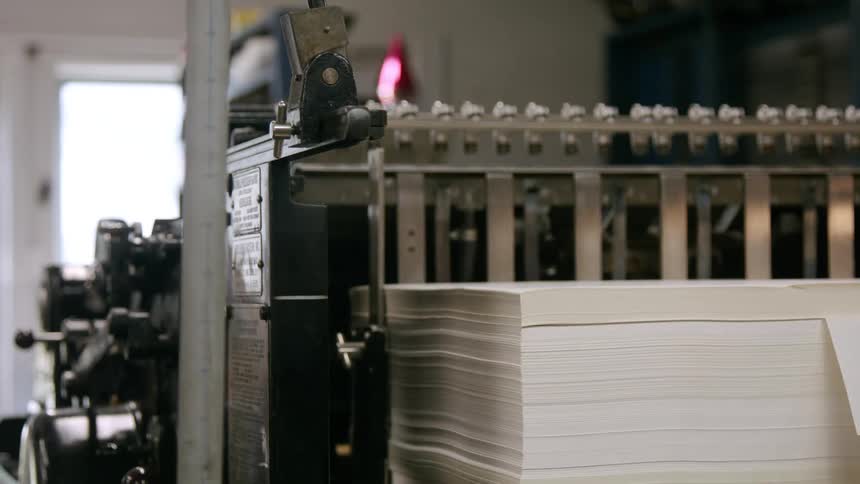 A workers hands pat down a tall stack of white papers to align them to begin the printing process